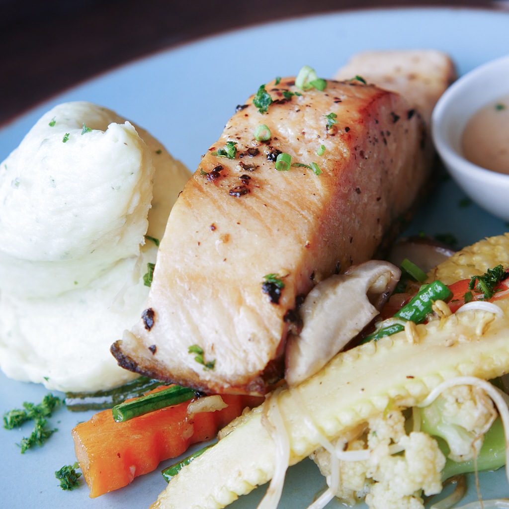 Cooked salmon sitting on top of vegetables on a light blue plate.